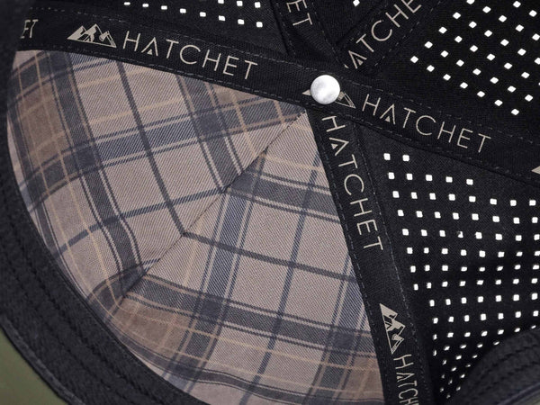 Close-up image of the interior of the Hunter Green colored Rover premium performance fitted hat from Hatchet Headwear. The interior of the hat features a black, tan, and brown plaid front panel liner, black seam tape with a taupe version of the Hatchet Headwear logo, and black sweatband featuring flex tech. Also visible in the image are diamond shaped laser perforations on the crown of the hat to provide breathability and reduce heat retention.