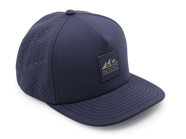 Slate Blue colored Rover premium performance fitted hat from Hatchet Headwear pictured with a white foreground and background. Hat features a color matched Slate Blue rubber logo patch with the Hatchet Headwear logo (mountains, tent, and hatchet above the word "HATCHET) in taupe. The hat is positioned at an approximately 45 degree angle to showcase the front and right-side profile of the hat. Image perspective of the hat is taken such that the hat is photographed from above.