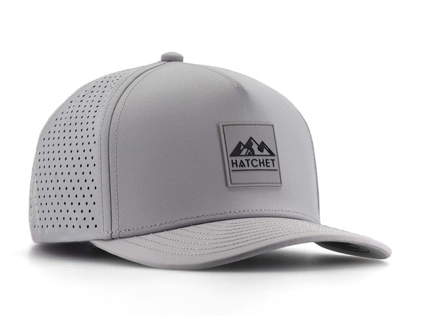 Smoke colored Rover premium performance fitted hat from Hatchet Headwear pictured with a white foreground and background. Hat features a color matched Smoke rubber logo patch with the Hatchet Headwear logo (mountains, tent, and hatchet above the word "HATCHET) in black. The hat is positioned at an approximately 30 degree angle to showcase the front and left-side profile of the hat.