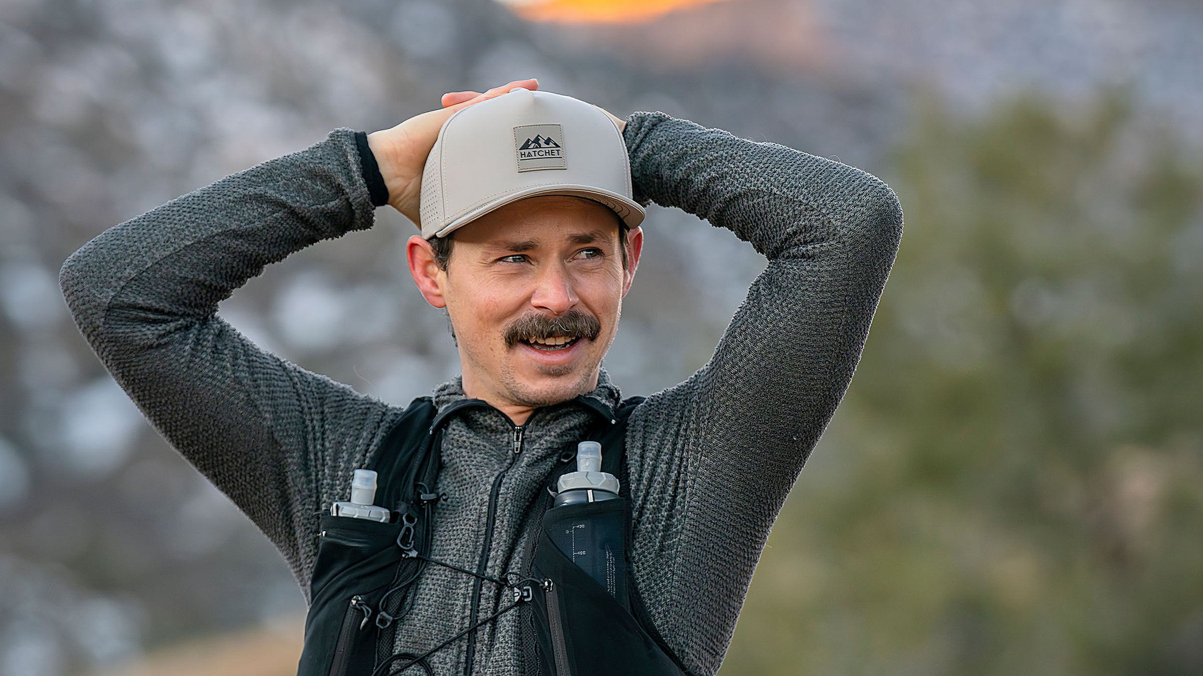 Man wearing a Boulder colored Rover premium performance fitted hat from Hatchet Headwear while taking a break from running in an outdoor environment.  Background of the outdoor environment is blurred.