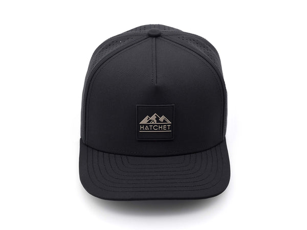Black colored Rover premium performance fitted hat from Hatchet Headwear pictured with a white foreground and background.  Hat features a color matched Black rubber logo patch with the Hatchet Headwear logo (mountains, tent, and  hatchet above the word "HATCHET) in taupe.  The hat is pictured from the front and facing directly at the camera.  Camera position is elevated and front facing image of the hat is captured from above.