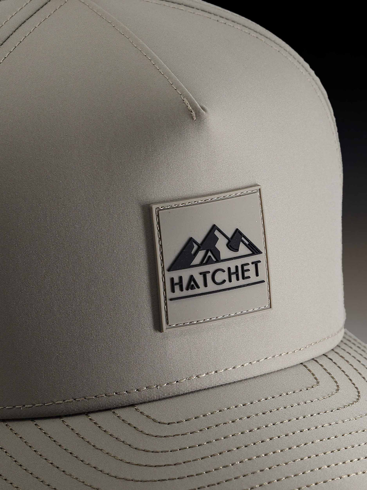 Close up photo of the front of a Boulder colored Rover premium performance fitted hat by Hatchet Headwear.  The close up photo depicts the stitching details and rubber Hatchet Headwear logo patch.