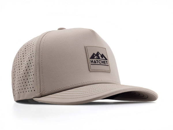 Boulder colored Rover premium performance fitted hat from Hatchet Headwear pictured with a white foreground and background.  Hat features a color matched Boulder rubber logo patch with the Hatchet Headwear logo (mountains, tent, and  hatchet above the word "HATCHET) in black.  The hat is positioned at an approximately 45 degree angle to showcase the front and right-side profile of the hat.  Image perspective of the hat is taken such that the hat is slightly above the camera lens position.