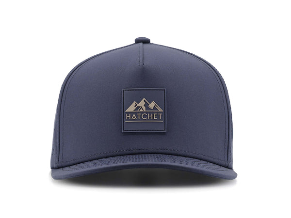Slate Blue colored Rover premium performance fitted hat from Hatchet Headwear pictured with a white foreground and background.  Hat features a color matched Slate Blue rubber logo patch with the Hatchet Headwear logo (mountains, tent, and  hatchet above the word "HATCHET) in taupe.  The hat is pictured from the front and facing directly at the camera.