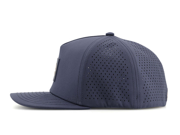Slate Blue colored Rover premium performance fitted hat from Hatchet Headwear pictured with a white foreground and background.  The hat is positioned at an approximately 90 degree angle to showcase the left-side profile of the hat.  The diamond shaped laser perforations of the hat designed to provide breathability and reduce heat retention are prominently featured.
