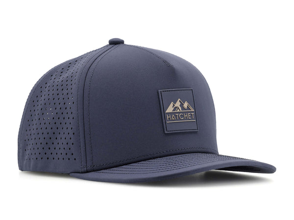 Slate Blue colored Rover premium performance fitted hat from Hatchet Headwear pictured with a white foreground and background.  Hat features a color matched Slate Blue rubber logo patch with the Hatchet Headwear logo (mountains, tent, and  hatchet above the word "HATCHET) in taupe.  The hat is positioned at an approximately 45 degree angle to showcase the front and right-side profile of the hat.