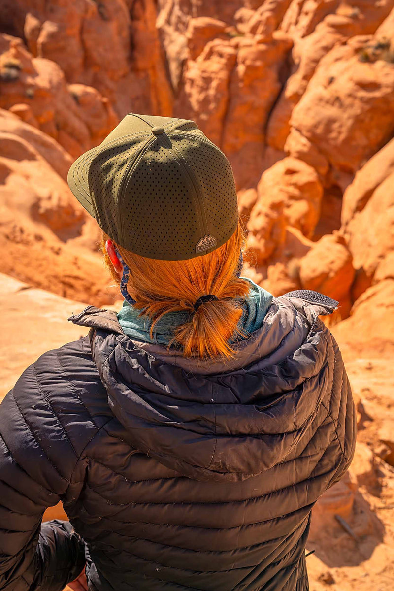 Man wearing a Hunter Green colored Rover premium performance fitted hat from Hatchet Headwear, navy blue jacket, blue shirt, and sunglasses while looking down into a red rock canyon.