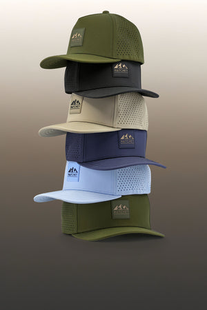 The six sizes of Hatchet Headwear hats stacked from the largest (bottom) to smallest (top) size.  Hat are sitting in front of a tan gradient background.  From bottom to top, the featured hat colors are Hunter Green, Glacier, Slate Blue, Boulder, Black, and Hunter Green.