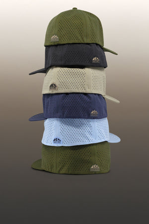 The six sizes of Hatchet Headwear hats stacked from the largest (bottom) to smallest (top) size.  Hat are sitting in front of a tan gradient background.  Rear of hats are visible to showcase the fitted style back closure.  From bottom to top, the featured hat colors are Hunter Green, Glacier, Slate Blue, Boulder, Black, and Hunter Green.