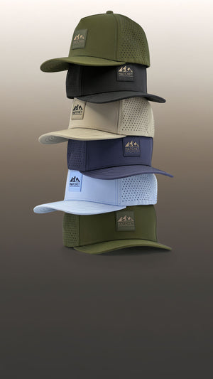The six sizes of Hatchet Headwear hats stacked from the largest (bottom) to smallest (top) size.  Hat are sitting in front of a tan gradient background.  From bottom to top, the featured hat colors are Hunter Green, Glacier, Slate Blue, Boulder, Black, and Hunter Green.